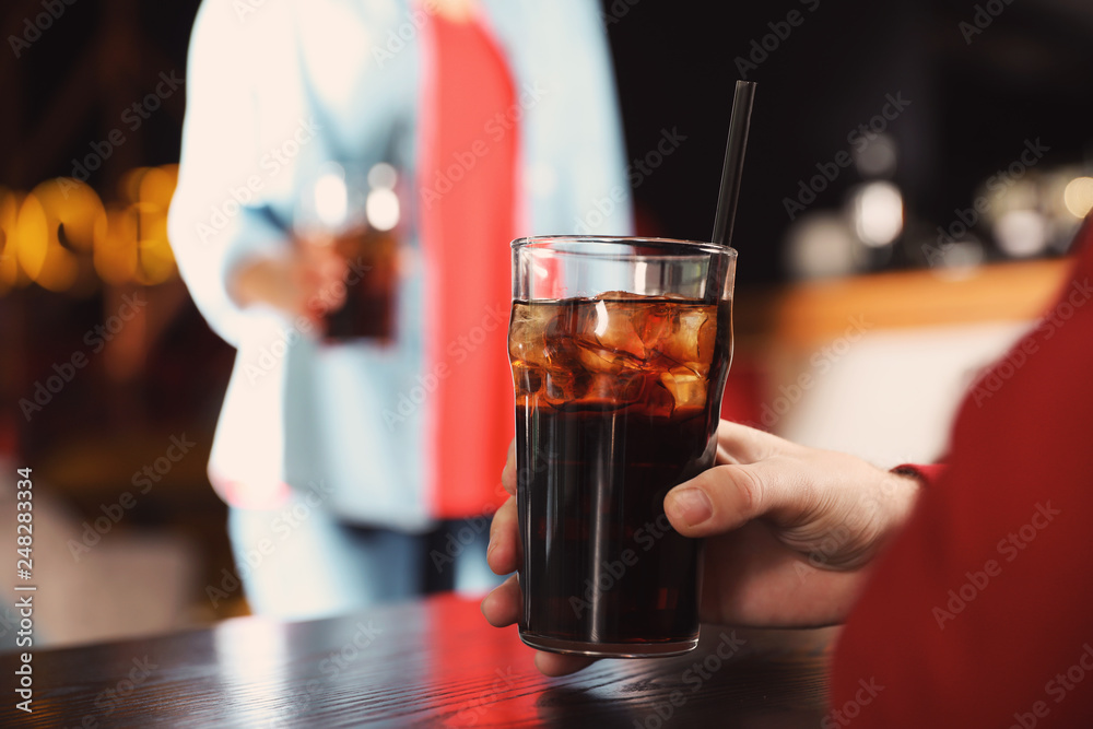 Man holding glass of cola at table in bar, closeup. Space for text