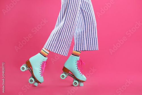 Young woman with retro roller skates on color background, closeup photo