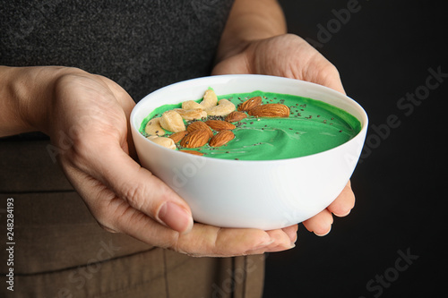 Woman holding bowl of spirulina smoothie with nuts and chia seeds, closeup