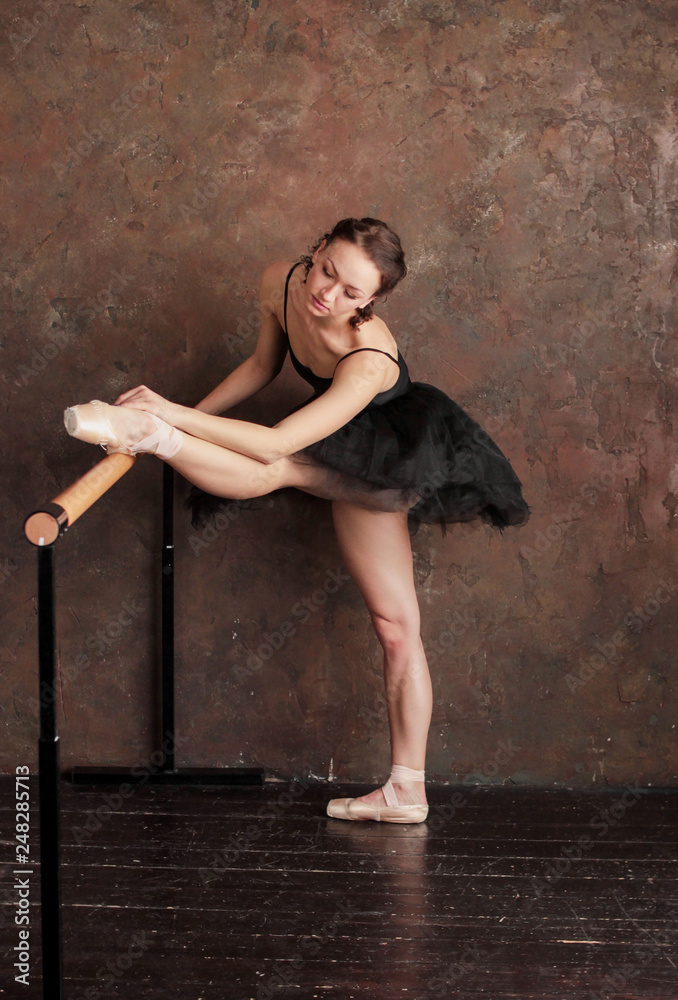 Ballet dancer ballerina in beautiful black dress tutu skirt is posing in loft studio