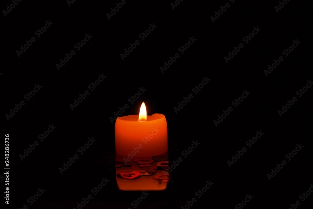 A lighted candle stands on the table. On the table are shiny colorful hearts. A lighted candle stands on the table. On the table are shiny colorful hearts.