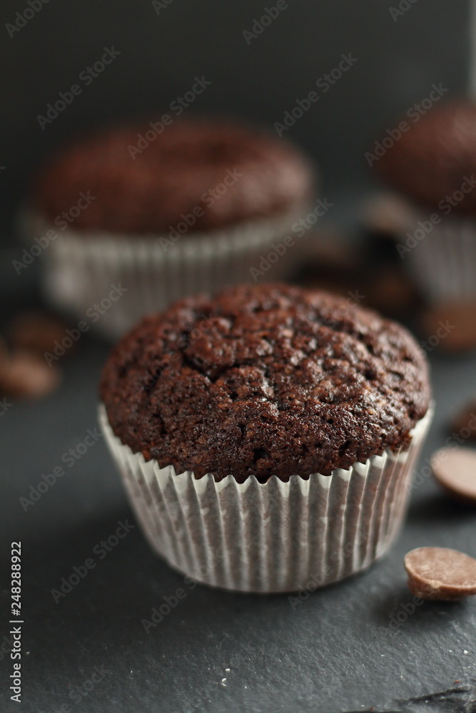 Chocolate homemade cupcakes muffins on a black background with chocolate drops in the background. Bakery style. Dark food photo vertical