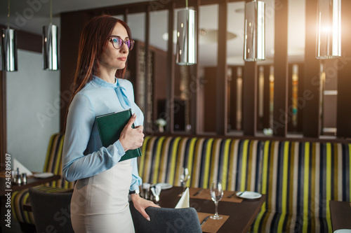Intelligent attractive middle-aged caucasian woman in silk blouse and pencil skirt, wearing glasses holding green notepad photo