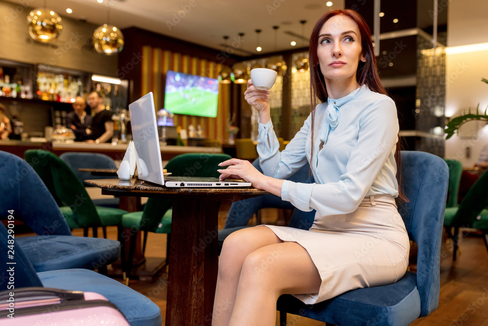 Pleasantly looking young woman with long ginger hair sitting in airport lounge, having tea and talking on mobile phone, leaving her country on business trip. Pleasantly looking young woman with long ginger hair sitting in airport lounge, having tea and talking on mobile phone, leaving her country on business trip.