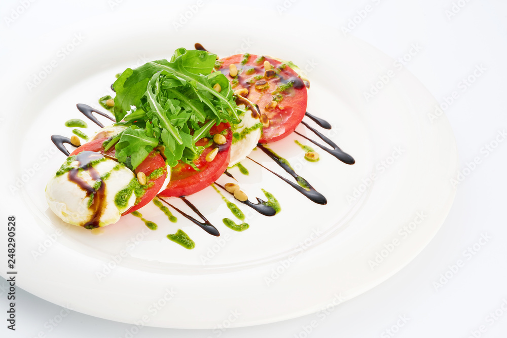 Mozarella cheese, tomatoes, arugula and pesto sauce in white plate. Mozarella cheese, tomatoes, arugula and pesto sauce in white plate.