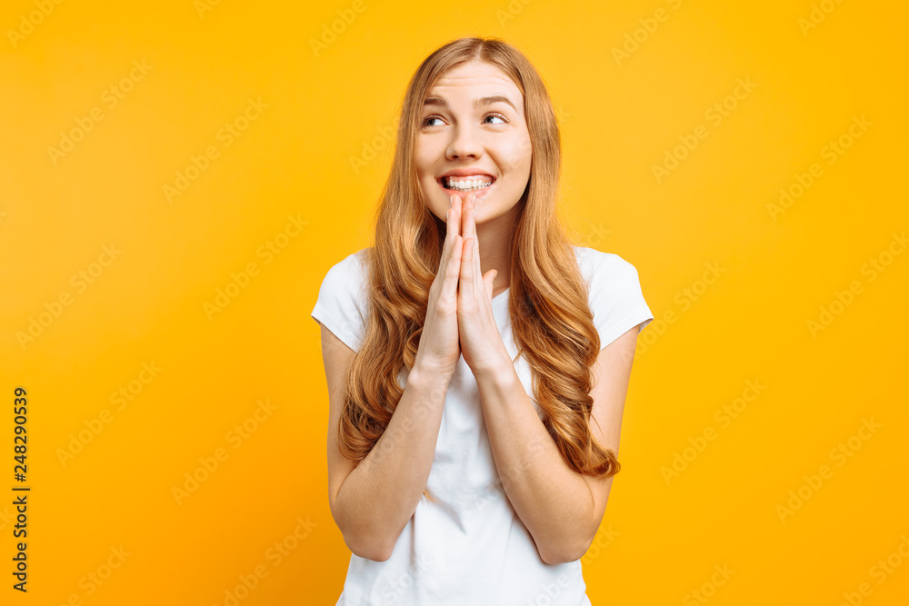 focused girl asks God to help her, holding hands near her face, wishes good luck, on a yellow background focused girl asks God to help her, holding hands near her face, wishes good luck, on a yellow background