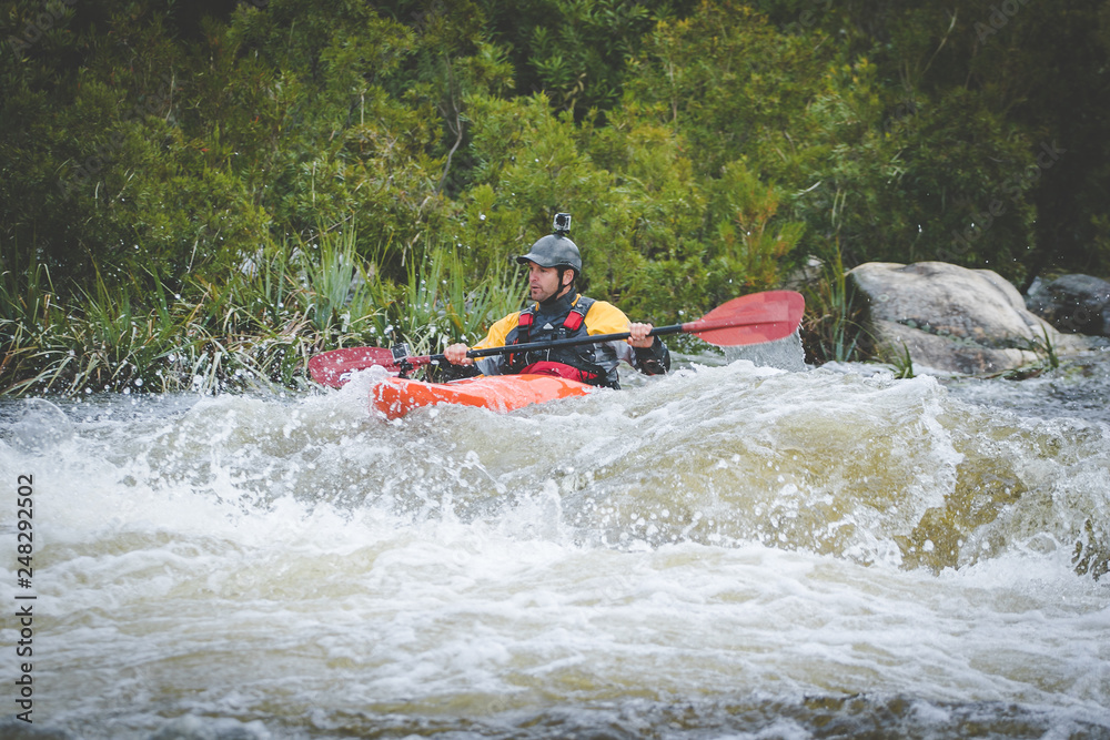 Close up image of a white water kayak paddler riding white water on a mountain river