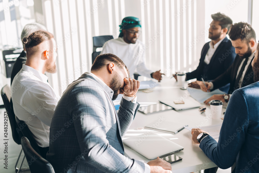Fototapeta premium Multiracial group of experts headed by Arab leader, dressed in national white wear, analyzing business result and discussing profit.