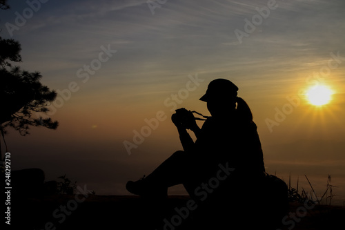 silhouette of a woman holding a camera taking pictures outside during sunrise or sunset