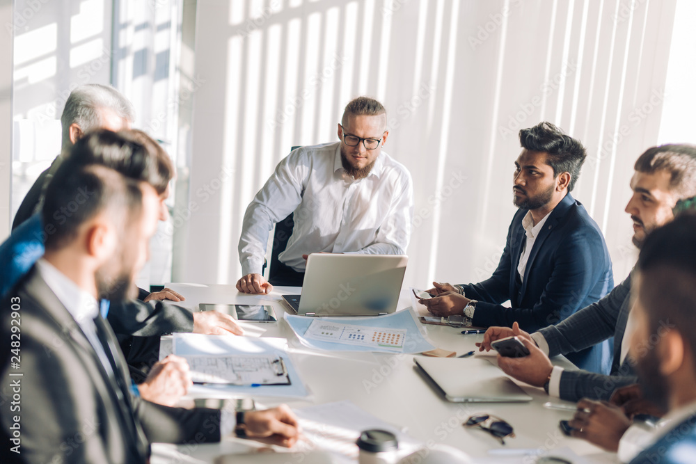 Fototapeta premium Happy optimistic middle-aged athletic business owner leading his team. Confident successful businessman and his multiracial colleagues in background. Successful team concept