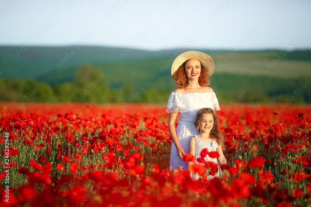 Mother with curly hair in a hat on a walk in the poppy field with her daughter. Mother with curly hair in a hat on a walk in the poppy field with her daughter.