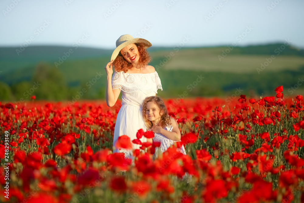 Mother and daughter in light dresses and hat walking on the farm field. Field of blooming poppies. Mother and daughter in light dresses and hat walking on the farm field. Field of blooming poppies.