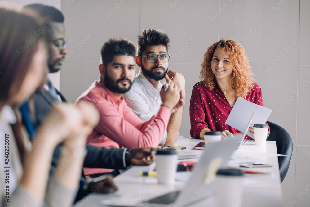 Mixed race diverse group of people in formal wear, sitting in raw at office table attending annual refresher course, led by a red-haired female coach Mixed race diverse group of people in formal wear, sitting in raw at office table attending annual refresher course, led by a red-haired female coach