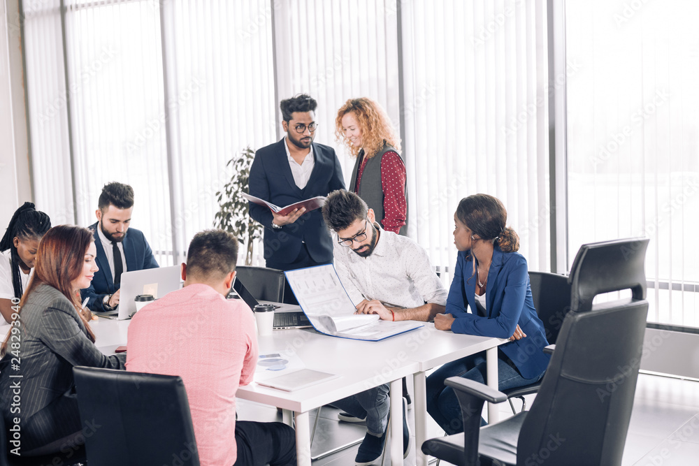 Coworking team meeting. Group of mixed-race diverse co-workers discussing new startup project in modern office with panoramic windows.