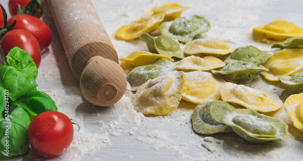 Fototapeta premium Homemade fresh Italian ravioli pasta on white wood table with flour, basil, tomatoes,background