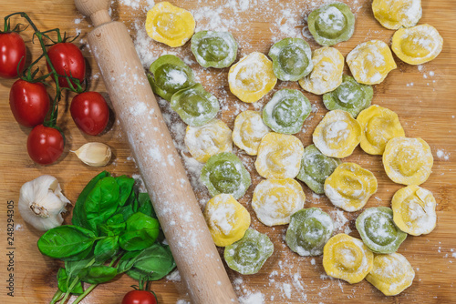 Homemade fresh Italian ravioli pasta on wood table  with flour  basil tomatoes background top view.