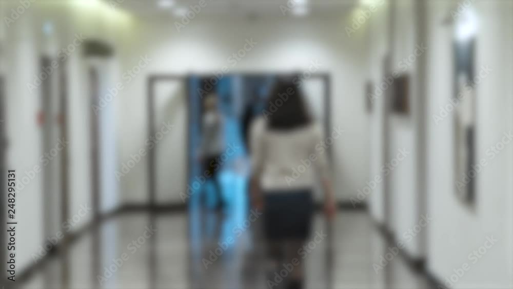 People walking down the hallway of a modern office building, blurred background.