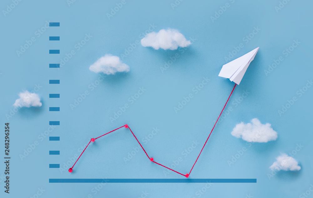 Fototapeta premium Conceptual paper plane pulling business finance growth chart line upwards on blue sky background. 