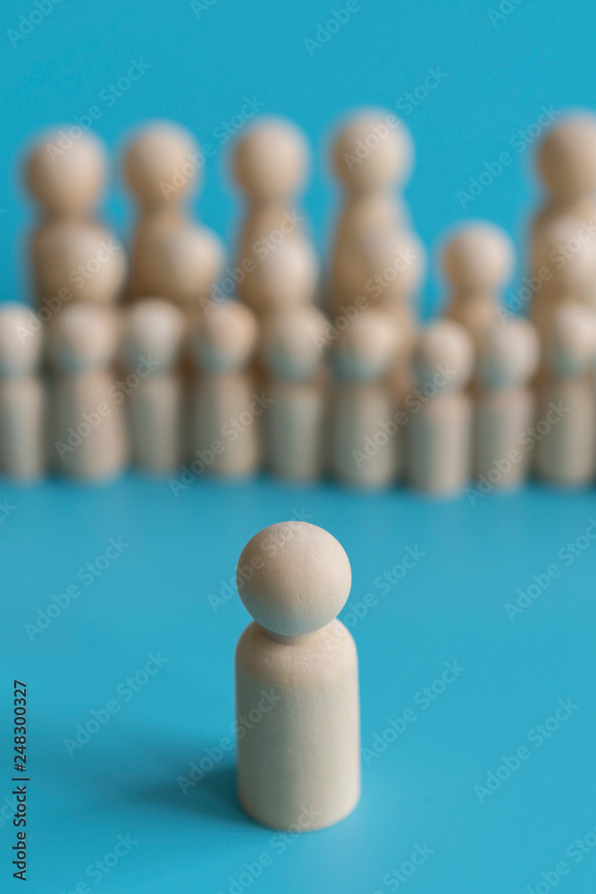 The concept of society. Stand out from the crowd, not like everyone else, leadership. Standing Out From The Crowd. Wooden figures on a blue background. vertical photo. The concept of society. Stand out from the crowd, not like everyone else, leadership. Standing Out From The Crowd. Wooden figures on a blue background. vertical photo.