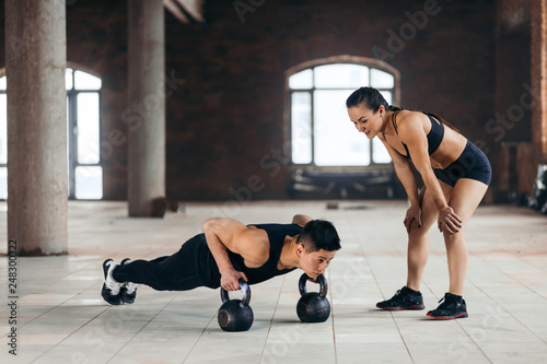 female personal trainer controlling a man who is doing push ups with kettlebells. woman encourages her boyfriend to go in for sport photo