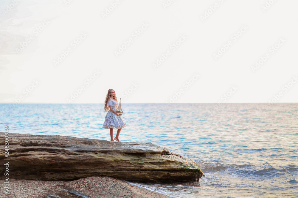 Portrait of a girl near the sea sitting on the rocks with a toy ship in hands. Portrait of a girl near the sea sitting on the rocks with a toy ship in hands.