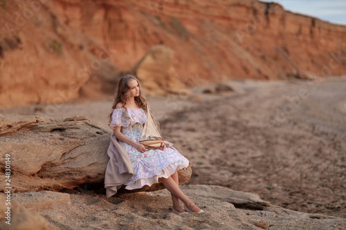 Portrait of a girl near the sea sitting on the rocks with a toy ship in hands.