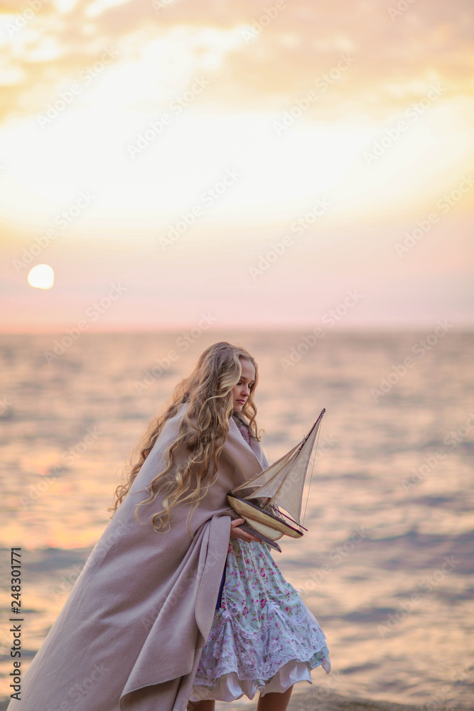 Portrait of a girl near the sea sitting on the rocks with a toy ship in hands. Portrait of a girl near the sea sitting on the rocks with a toy ship in hands.
