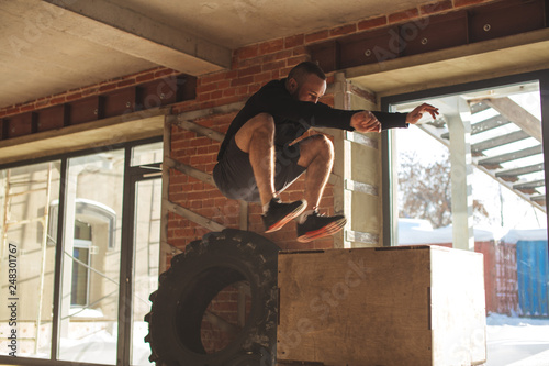 Young male Athlete doing plyo jumps exercise training endurance in crossfit gym. Jumping on the box. Phase touchdown. photo