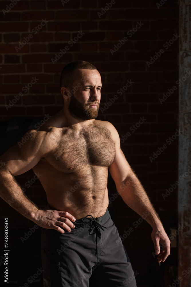 Portrait of strong healthy bearded athletic man with naked torso posing against dark wall looking aside