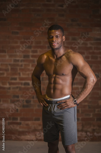 Strong afroamerican athletic man with naked perfect shape musculs looking at camera isolated over brick background.