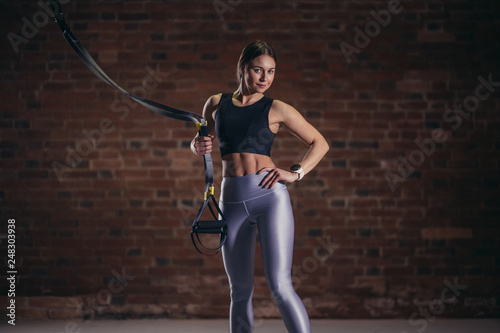 Sports Girl looking at camera while engaging in TRX functional workout in loft style gym.