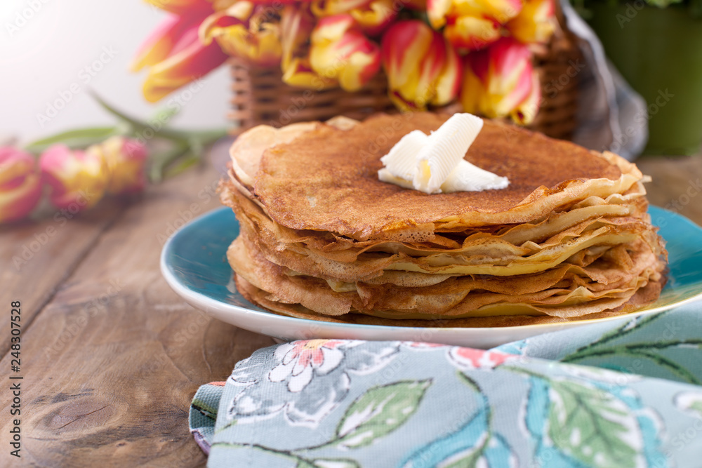 Russian pancakes with butter on a wooden background. A bouquet of fresh spring tulips and traditional Russian food. Free space for text.