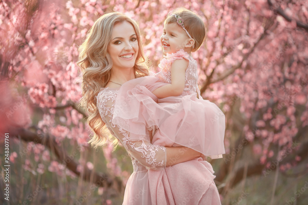 Portrait of young beautiful mother with her little girl. Close up still of loving family. Attractive woman holding her child in pink flowers and smiling Portrait of young beautiful mother with her little girl. Close up still of loving family. Attractive woman holding her child in pink flowers and smiling