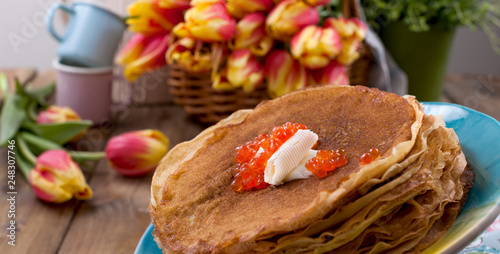 pancakes with caviar and butter, a bouquet of fresh tulips and a wooden background. Traditional Russian food for carnival. Top view.
