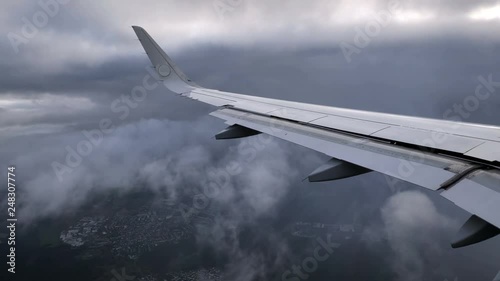 Wing of landing airplane or jet on storm gray sky background and fluffy clouds on moving. Aerial view from high on rainy cloudy day. Real time footage