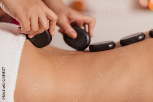 talented beautician massaging girl s back. close up cropped photo. spa tratment with magic stones