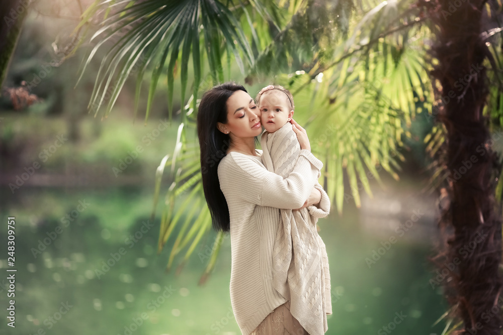 Naklejka premium Young and happy mother cares for her young son, and walks along the shore of the lake in the summer in the park
