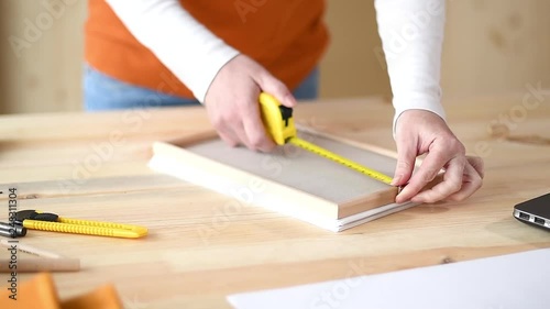 Female carpenter tape measuring picture frame in small business woodwork workshop, close up of hands