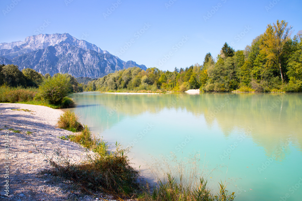 Idyllic shore landscape with pebble beach, blue water, flowers and mountains