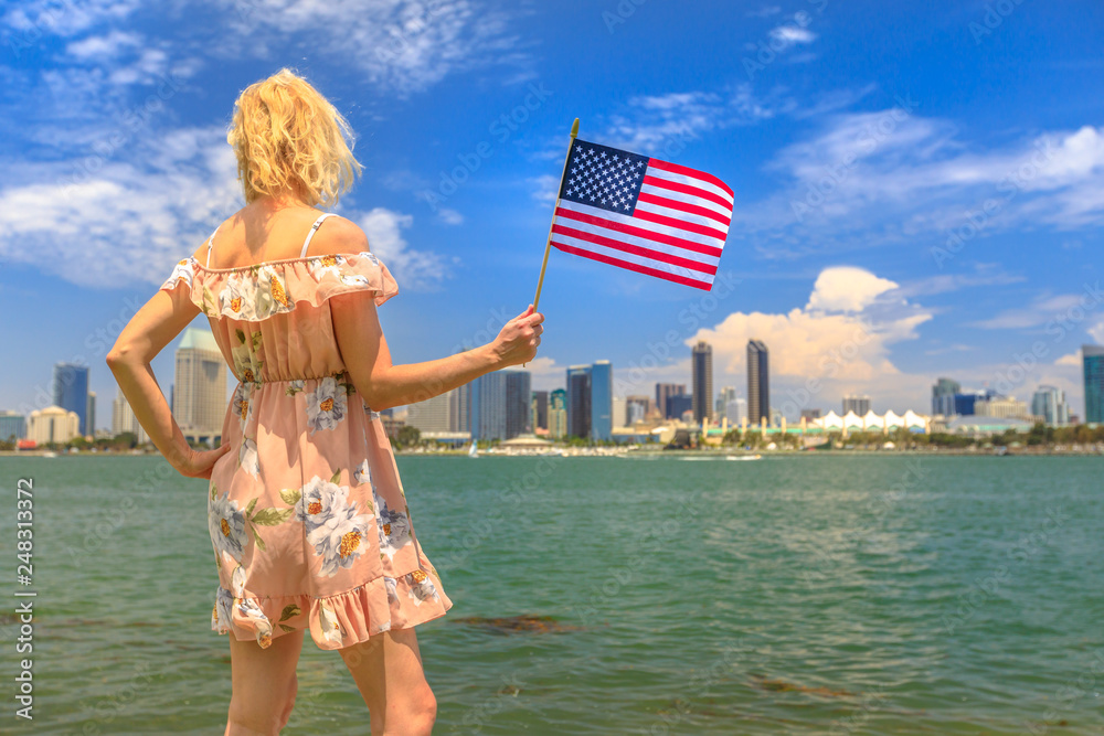 Tourism and travel in California, West Coast, USA. Blonde lady looking San  Diego skyline with American flag waving from Coronado Island. Tourist woman  in summer holidays. Cityscape in San Diego Bay. Stock