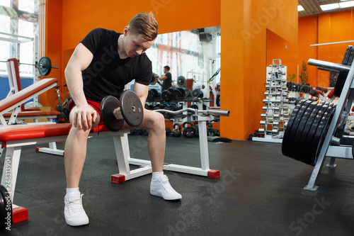 Young, athletic guy lifting dumbbells in the gym.