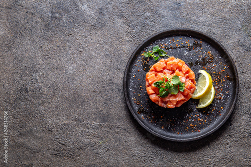 Raw salmon, avocado purple onion salad served in culinary ring on black plate. Black concrete background