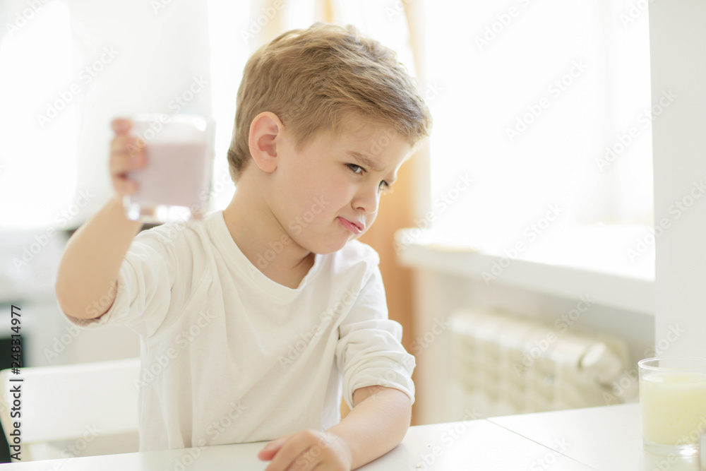 Kid or blonde happy boy eating at table. Childhood and happiness, independence. Breakfast, morning, family. Small boy child eat banana and drink milk. Healthy food and vitamin. dieting, vegetarian Kid or blonde happy boy eating at table. Childhood and happiness, independence. Breakfast, morning, family. Small boy child eat banana and drink milk. Healthy food and vitamin. dieting, vegetarian