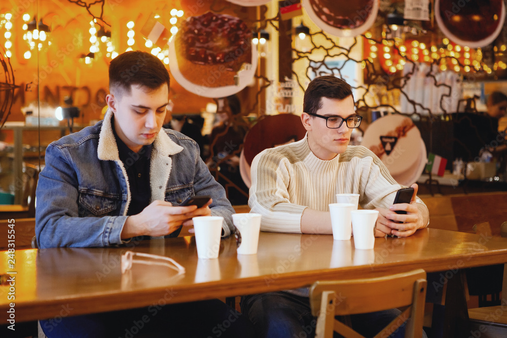 Portrait of cheerful young friends looking at smart phone while sitting in cafe. Mixed race people sitting at a table in restaurant using mobile phone.