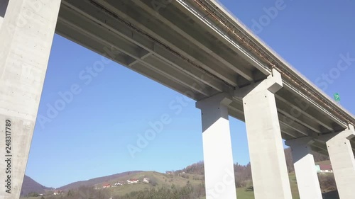 Aerial: Filming big highway concrete viaduct bridge concrete pilars. Filming highway concrete viaduct bridge over green valley on spring sunny day.