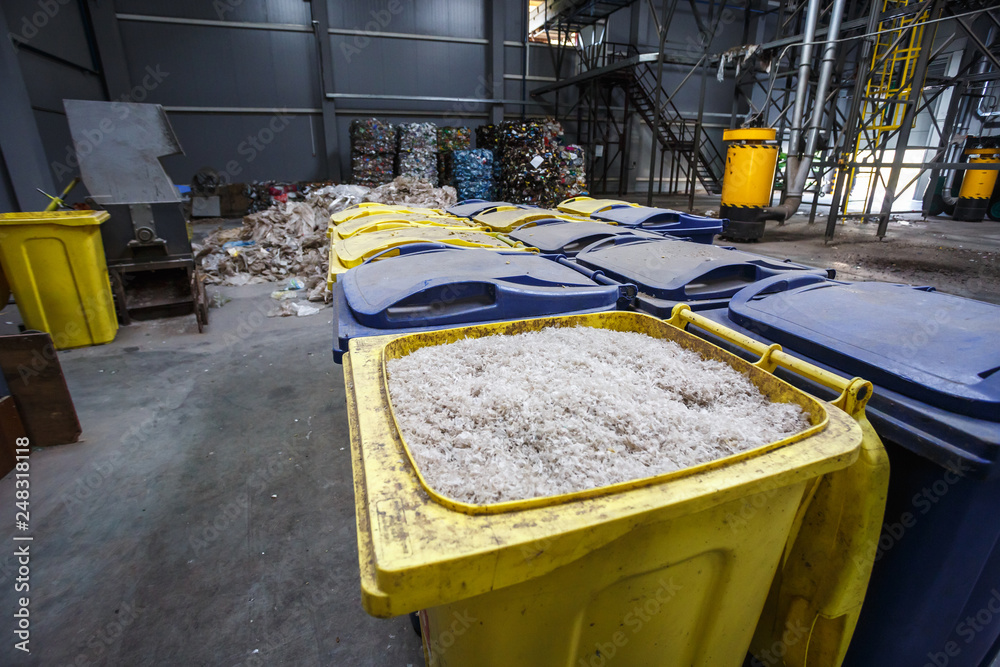Containers with shredded plastic prepared for further processing remelting and recycling with shredder and bales of plastic waste in the background. Modern plant for processing and sorting garbage Containers with shredded plastic prepared for further processing remelting and recycling with shredder and bales of plastic waste in the background. Modern plant for processing and sorting garbage