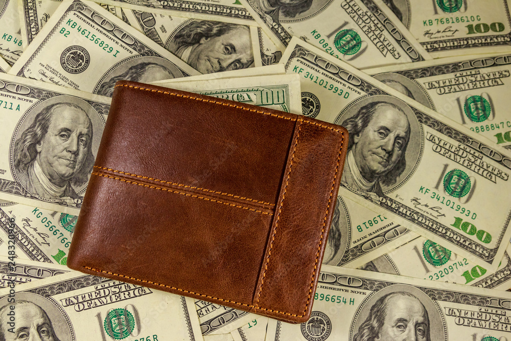 Brown leather wallet on the american one hundred dollar bills background Brown leather wallet on the american one hundred dollar bills background