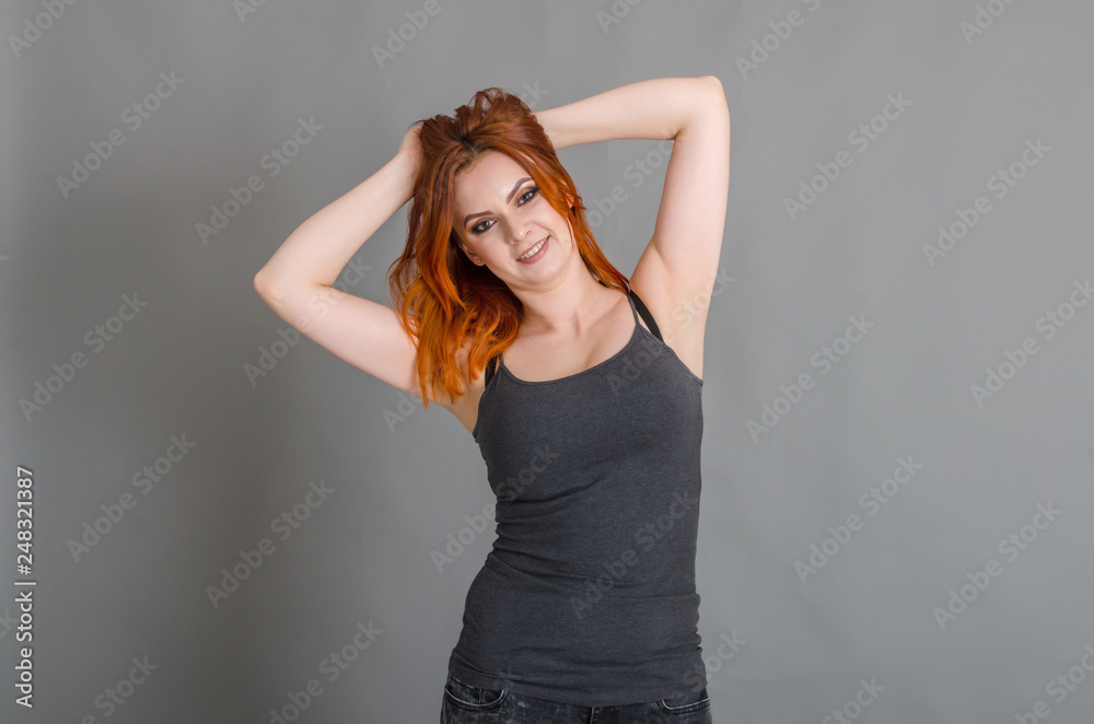 Attractive woman with red hair in a gray tank top posing on a dark blue background. Women's health, beauty, style Attractive woman with red hair in a gray tank top posing on a dark blue background. Women's health, beauty, style