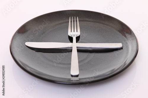 白いテーブルに置かれた黒い皿とカトラリーによる次の料理を待機の合図