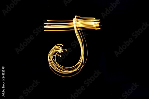 Long exposure, light painting photography. Letter j in a vibrant neon metallic yellow gold colour against a black background. Alphabet series.
